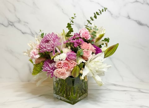 Floral arrangement with pink, purple, and white flowers in a glass vase on marble background