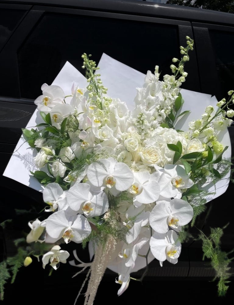 Elegant white flower bouquet with orchids, roses, and greenery wrapped in white paper against a dark background