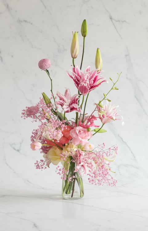 Pink floral arrangement in glass vase with carnations, lilies, and babys breath on marble background