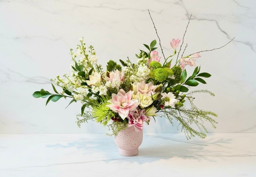 Elegant floral arrangement with pink roses, white flowers, green foliage, and branches in a beige ceramic vase on marble background
